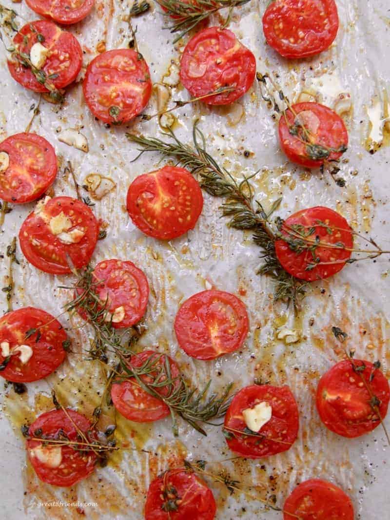 Fresh tomatoes, rosemary, thyme, and garlic on parchment covered sheet pan after roasting for 15 minutes.