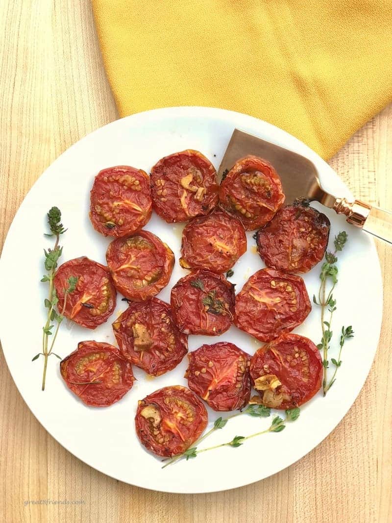 Roasted tomatoes on a plate with a serving spatula and fresh thyme.