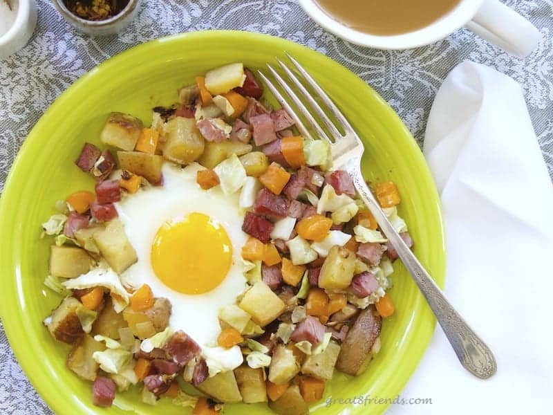 Overhead shot of corned beef hash with a sunny side up egg in the center. On a lime green plate with a silver fork.