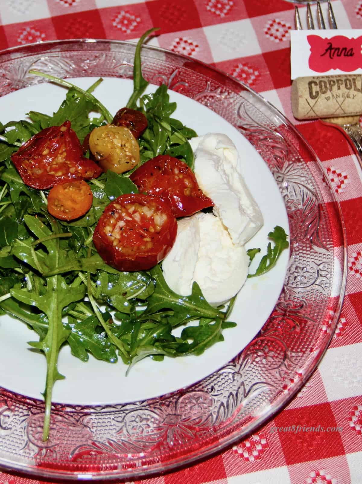 An arugula and fennel salad with roasted tomatoes and mozzarella on a red and white tablecloth.