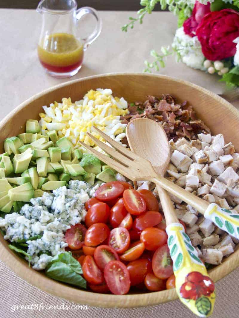 Cobb Salad with dressing in background and salad servers laying on top.