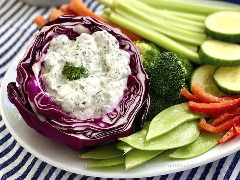 A plate of fresh veggies with Herby Dill Dip served from a hollowed out red cabbage.