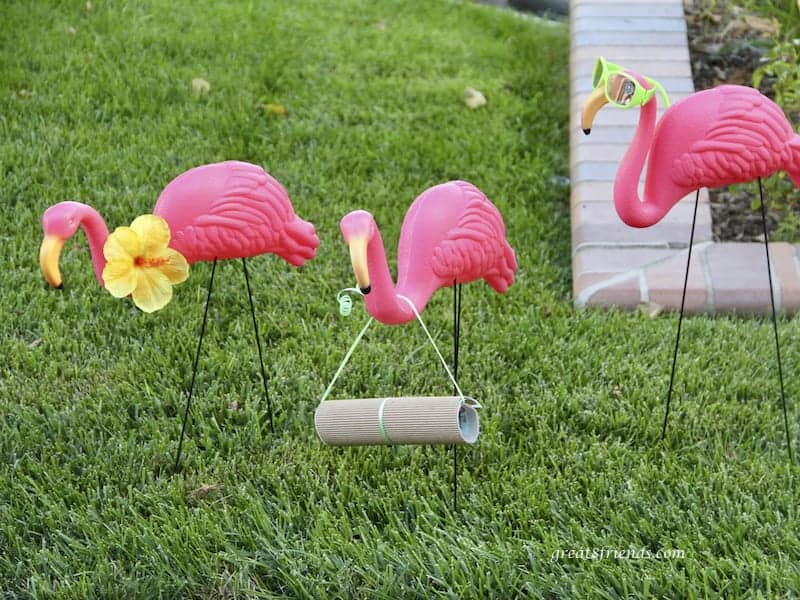 3 pink plastic flamingoes on grass one is holding a rolled up invitation to the Hot Havana in Miami dinner.