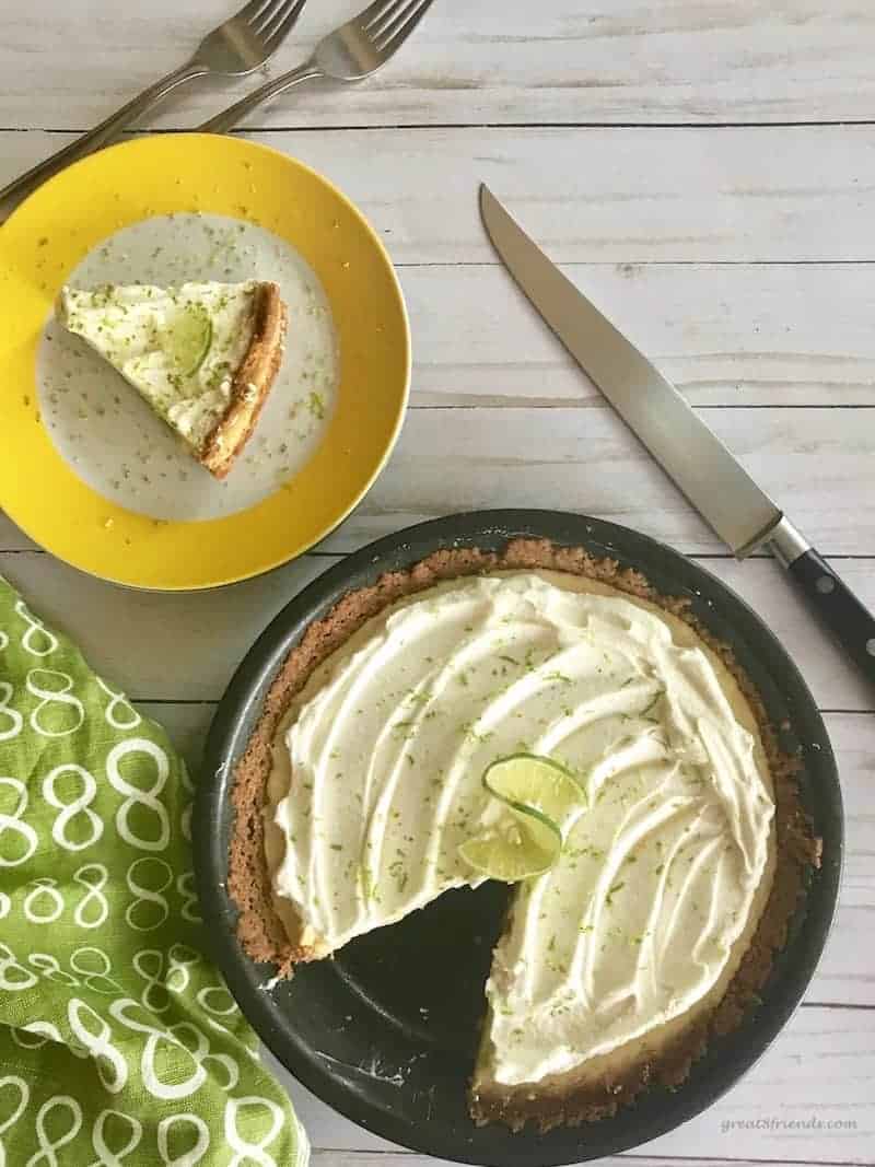 Key lime pie with one piece cut out and on a yellow and white plate with a knife on the side and a green and white napkin.