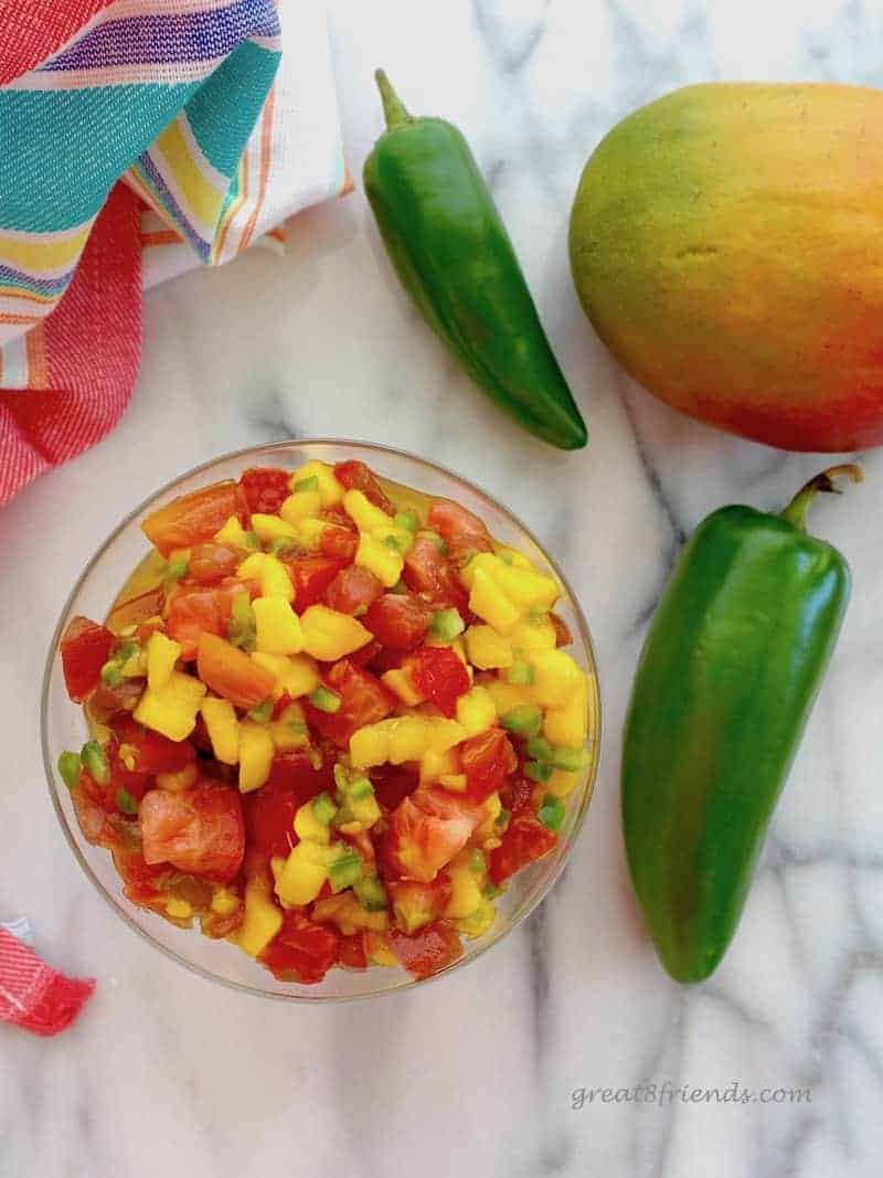 Overhead shot of Mango Papaya Salsa on marble with a couple of jalapenos and mango.