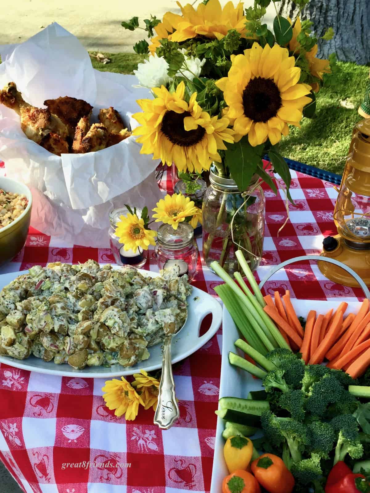 Red and White checked tablecloth set with sunflowers and picnic food.