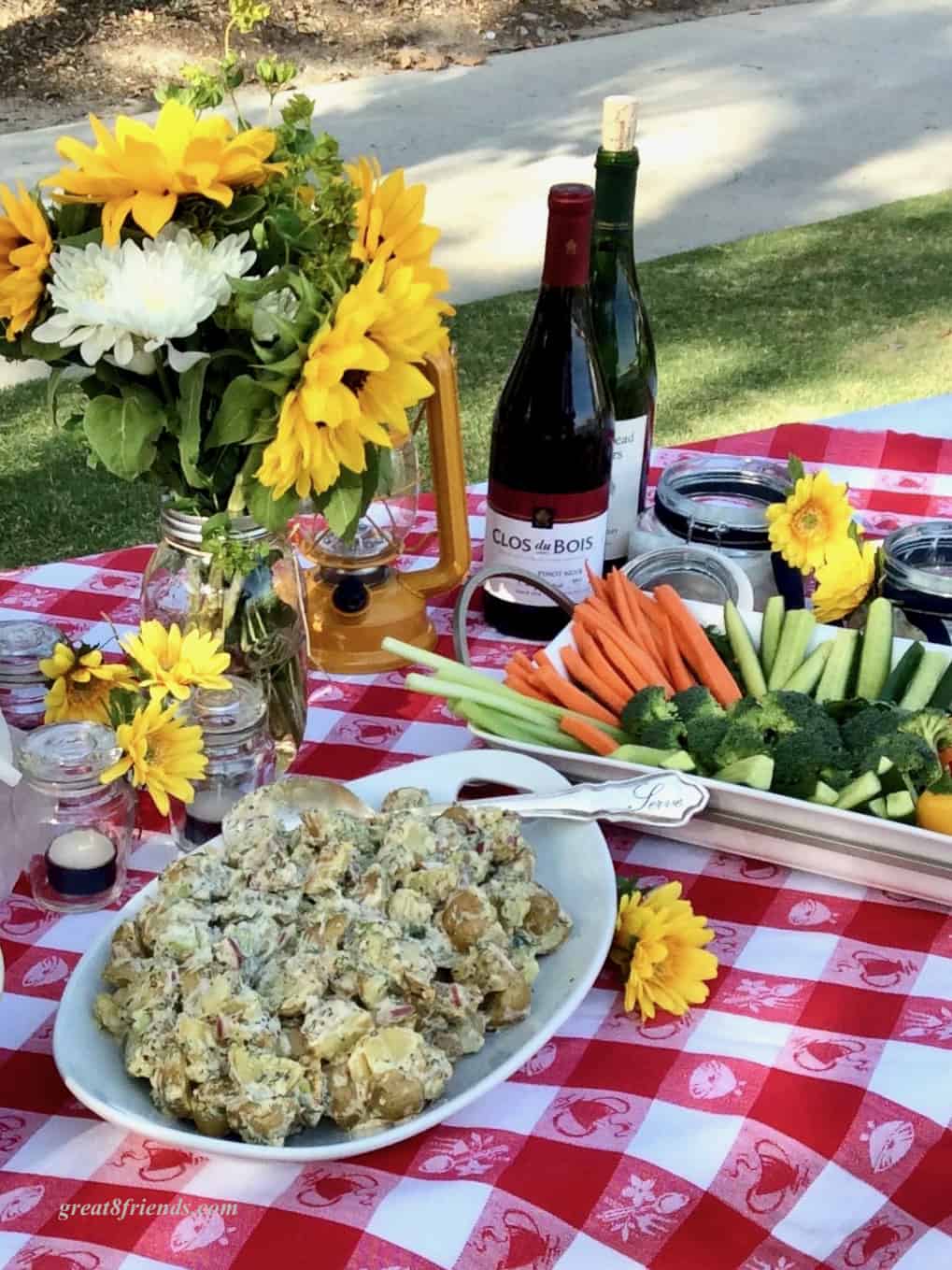 Red and White checked tablecloth set with sunflowers and picnic food.