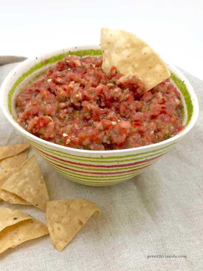A green striped bowl of salsa fresca with a tortilla chip stuck in it.