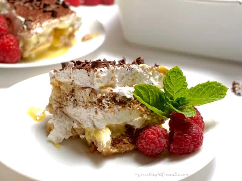 Tiramisu on a plate garnished with raspberries and mint.