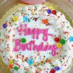 Overhead shot of white frosted cake with pink Happy Birthday writing.