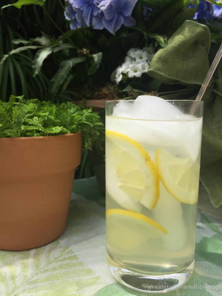 Fresh lemonade in a tall glass with ice and slices of lemons floating in the glass.