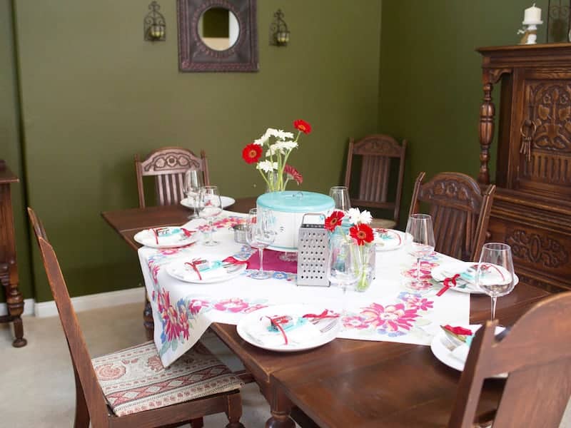 Memories from our Mother's Kitchen Dining Table set with vintage red and white flowered tablecloth. A vintage metal cake carrier is the centerpiece.