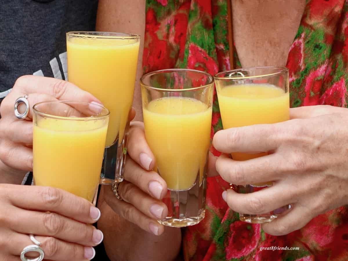 Four hands toasting glasses containing mimosas.