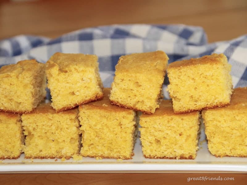 Stacked cut pieces of cornbread on rectangular platter with a blue checked cloth in the background.