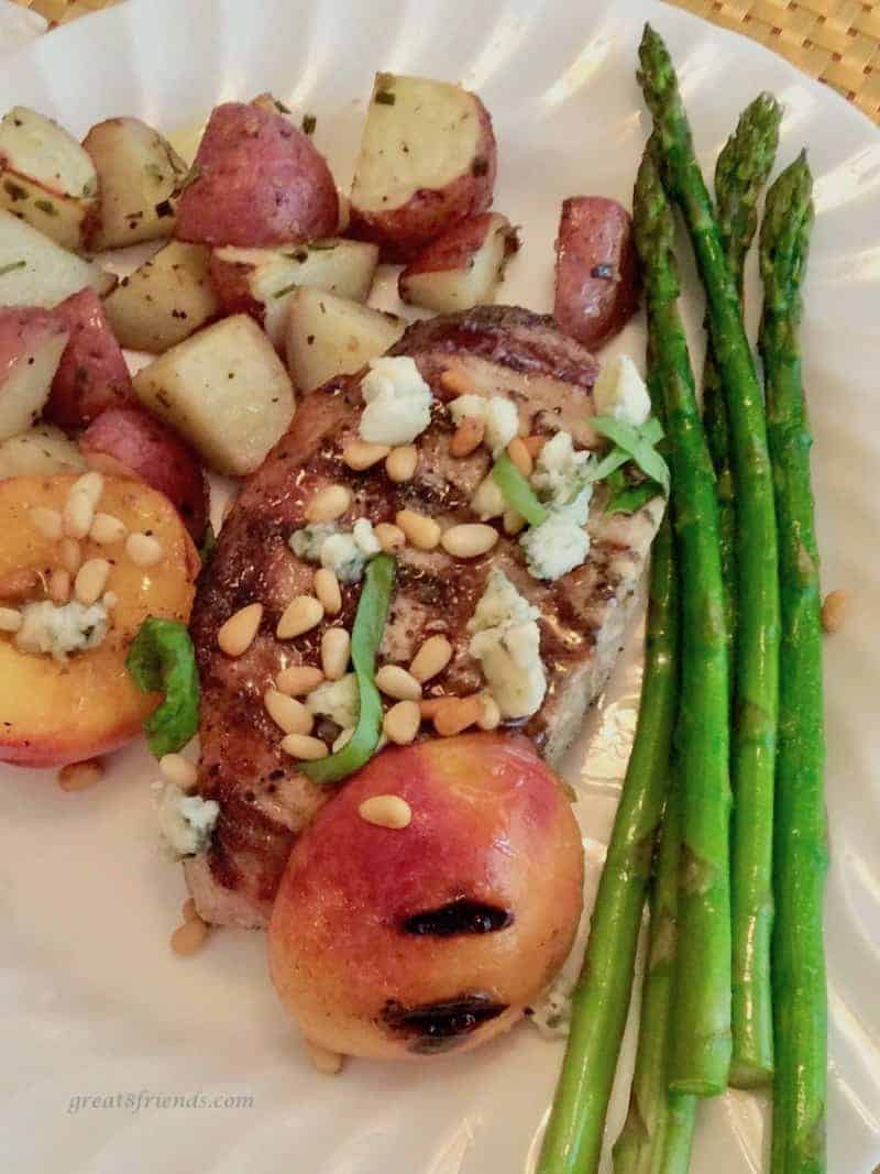 White dinner plate with a grilled pork chop, grilled nectarine halves, red potatoes and asparagus along the side.