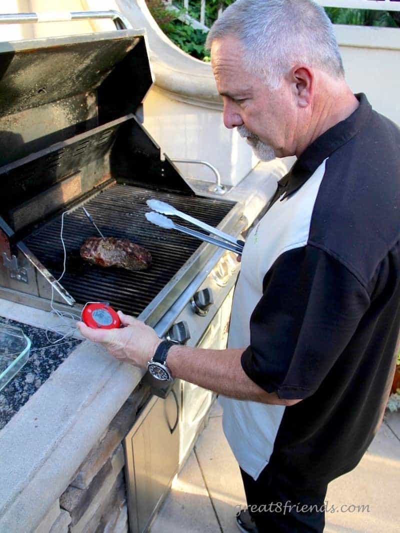 Man at grill cooking steak and looking at thermometer to ensure meat safety.