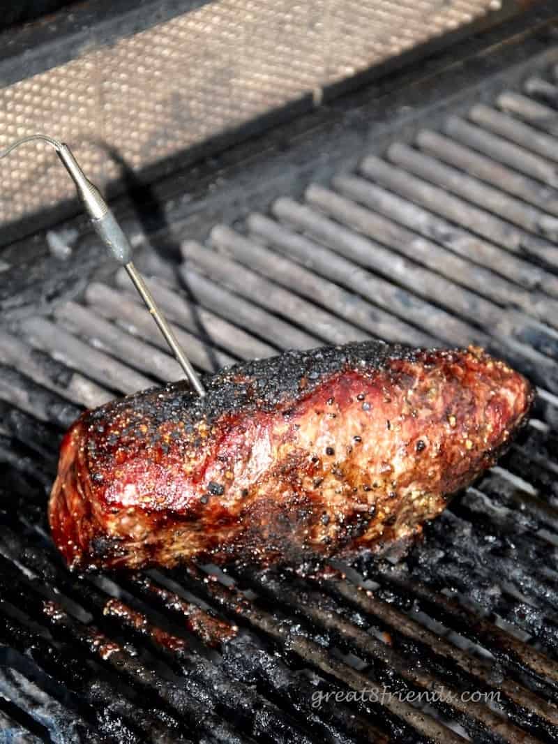 Steak on grill with thermometer sticking out of it to ensure meat safety.