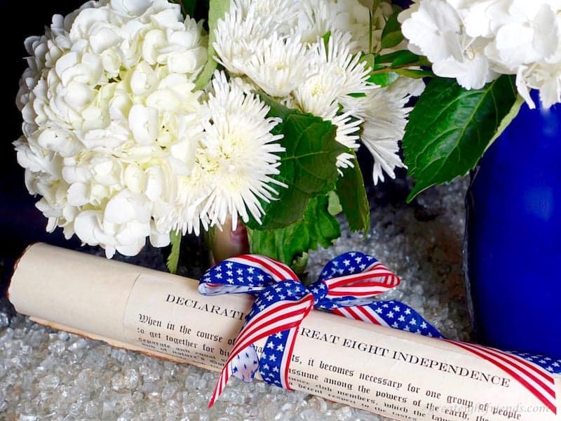 A scroll tied with a red, white and blue ribbon and a bouquet of white flowers.