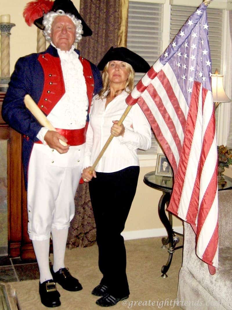 A man and woman dressed in revolutionary war costumes holding a large American Flag.