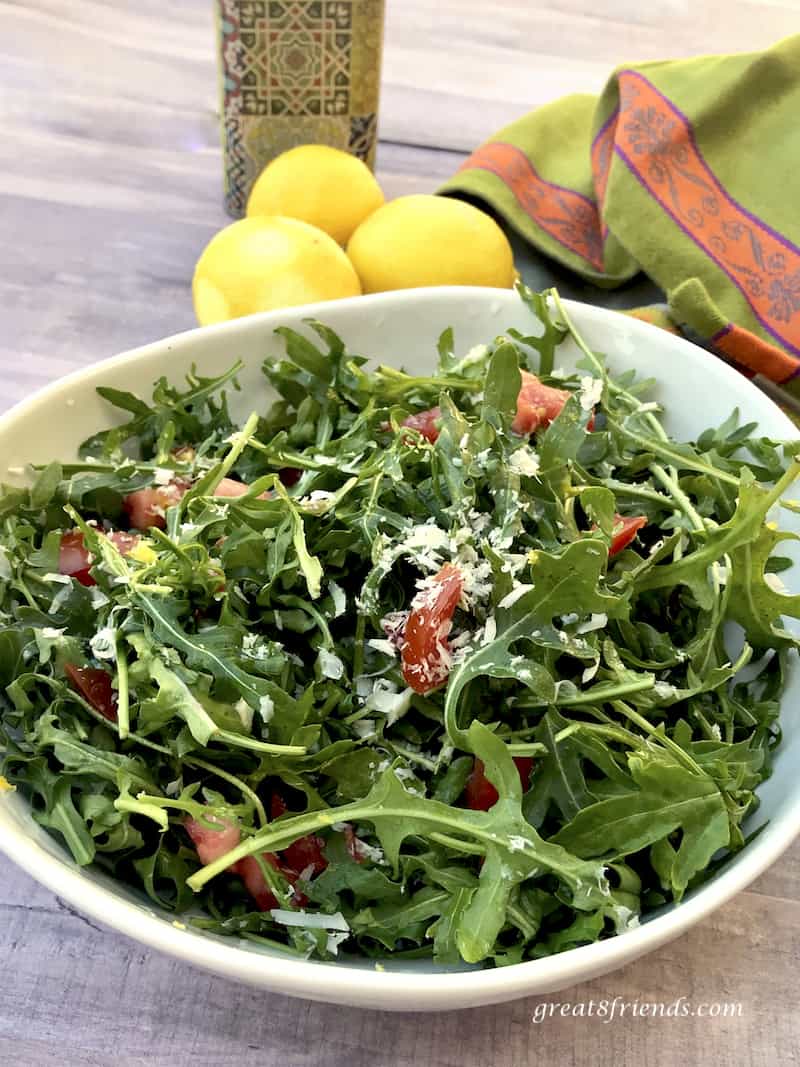 Arugula Salad with Lemon Parmesan Dressing in bowl with zested lemons and green and orange towel.