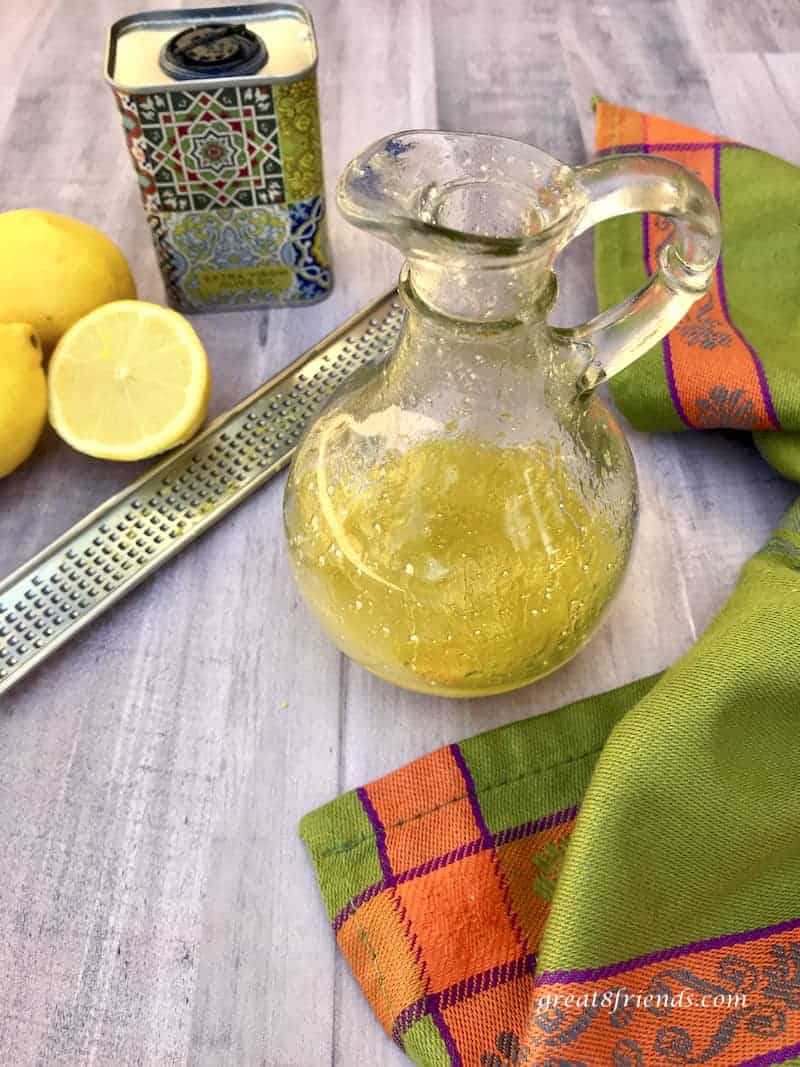 Lemon Parmesan Dressing in glass cruet with lemons, zester and olive oil.