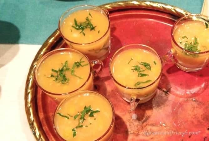 Yellow Tomato Soup in glass cups sitting on a round copper tray.