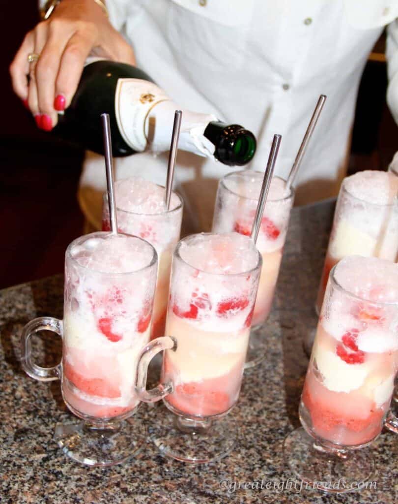 Champagne being poured into glasses containing strawberries and ice cream.