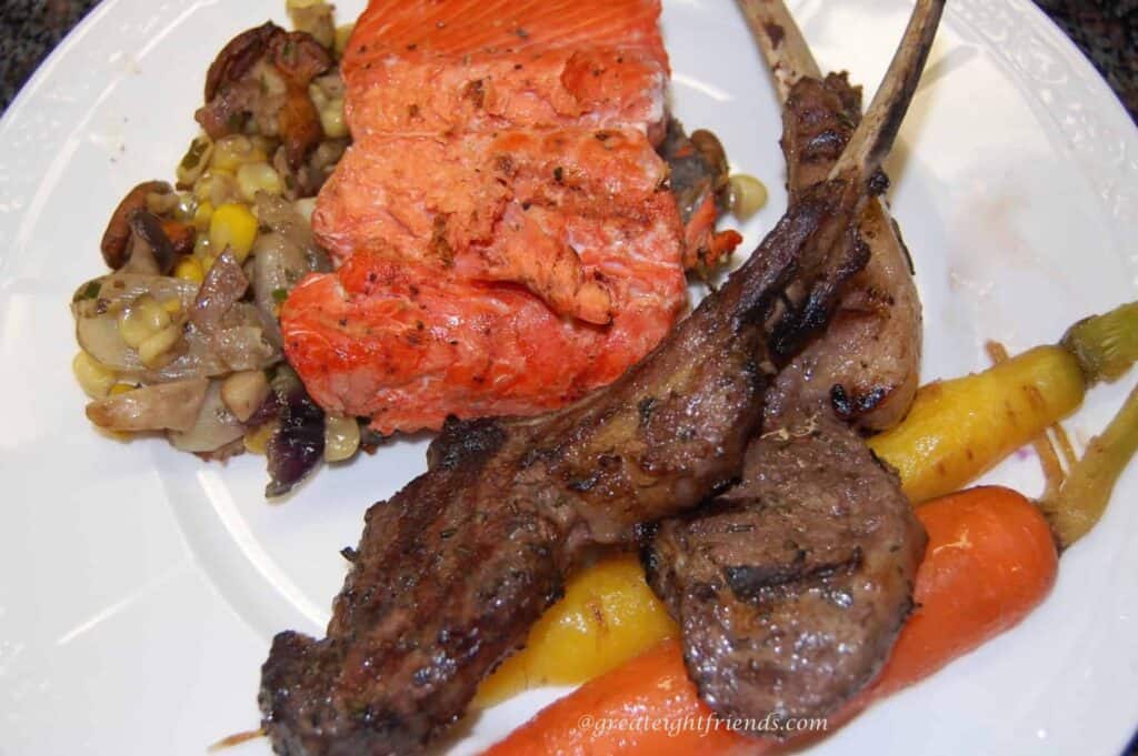 A plate with 2 lamb chops, salmon and some veggies.