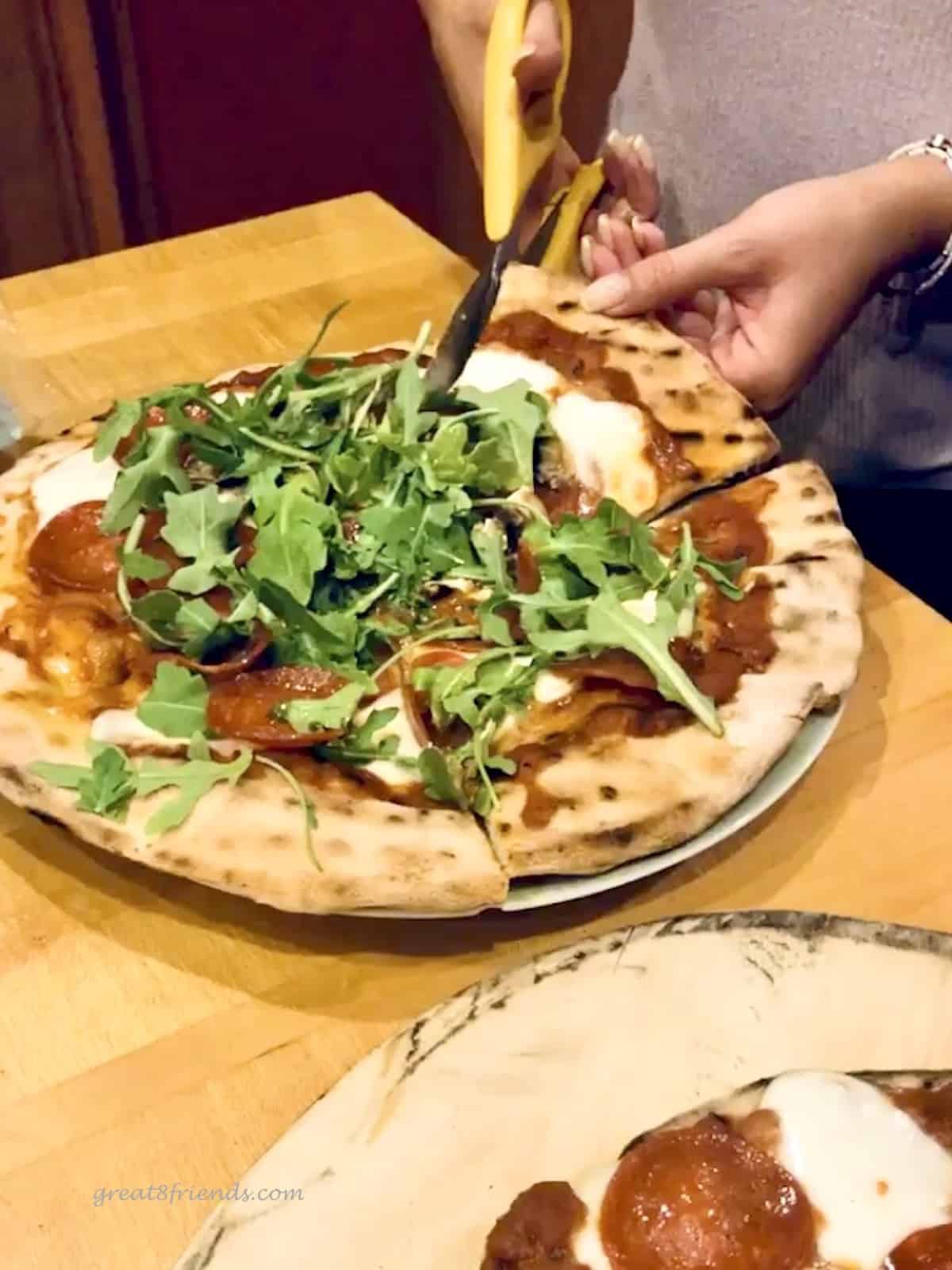 Pizza with arugula topping being cut with scissors.