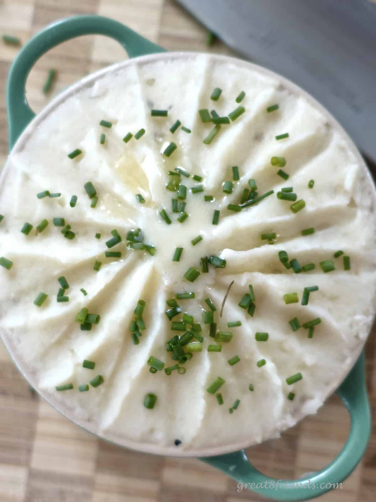 Overhead shot of mashed potatoes garnished with chopped chives. The top of these Pomme de Terre Robuchon is fluted with a knife edge to create texture.