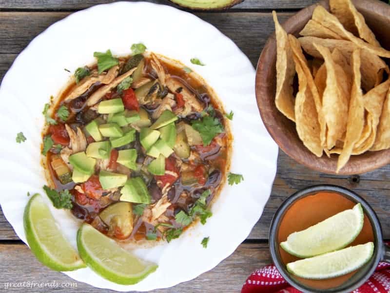 Chicken tortilla soup topped with avocado and served with limes.