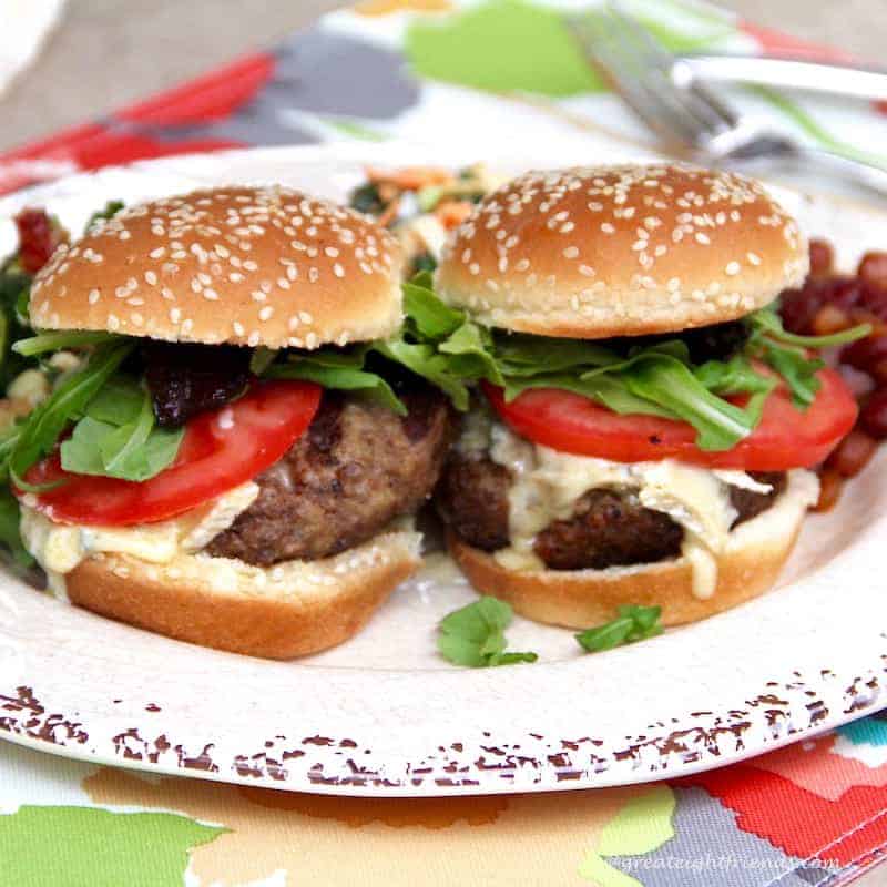 Two Cambozola beef sliders with Bacon Jam, arugula and tomatoes on a sesame seed buns.