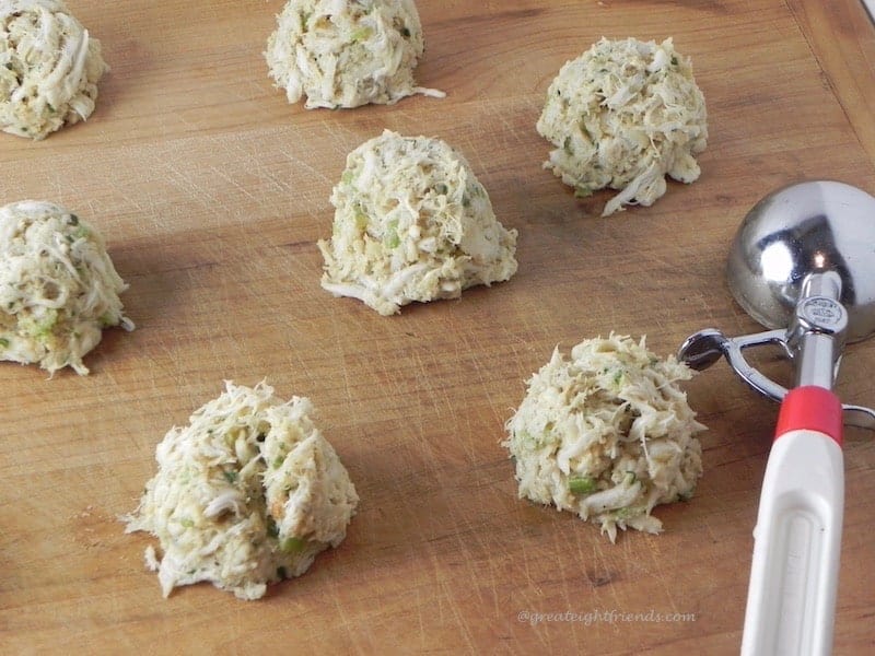 Uncooked Crab Cakes in mounds on a board, not yet flattened for cooking. An ice cream scoop on the side.