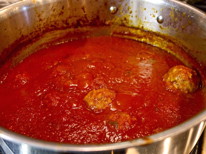 A pot of red sauce cooking with some meatballs. 