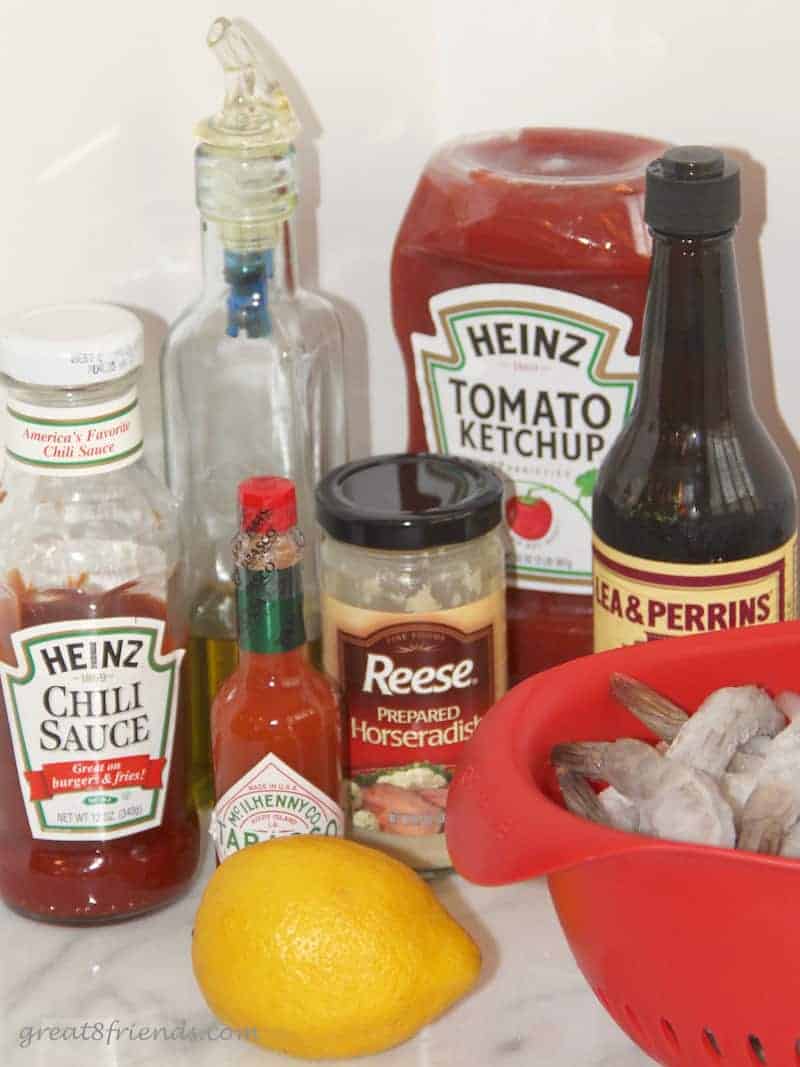 All the ingredients to make cocktail sauce: ketchup, chili sauce, tabasco, horseradish, Worcestershire sauce, lemon and raw shrimp in a bowl.