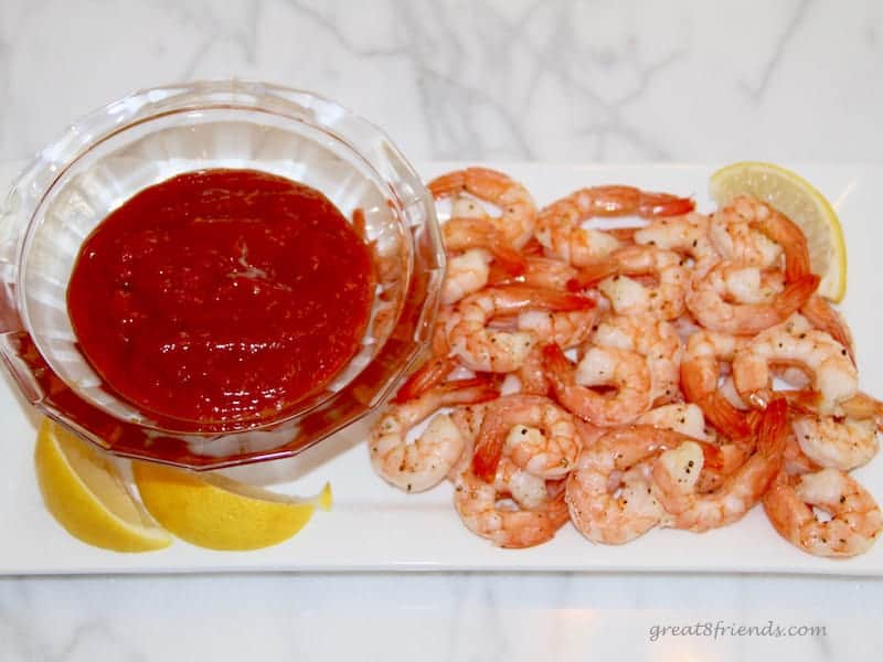 This Roasted Shrimp and sauce in a bowl being served on a white plate with lemon wedges on the side.