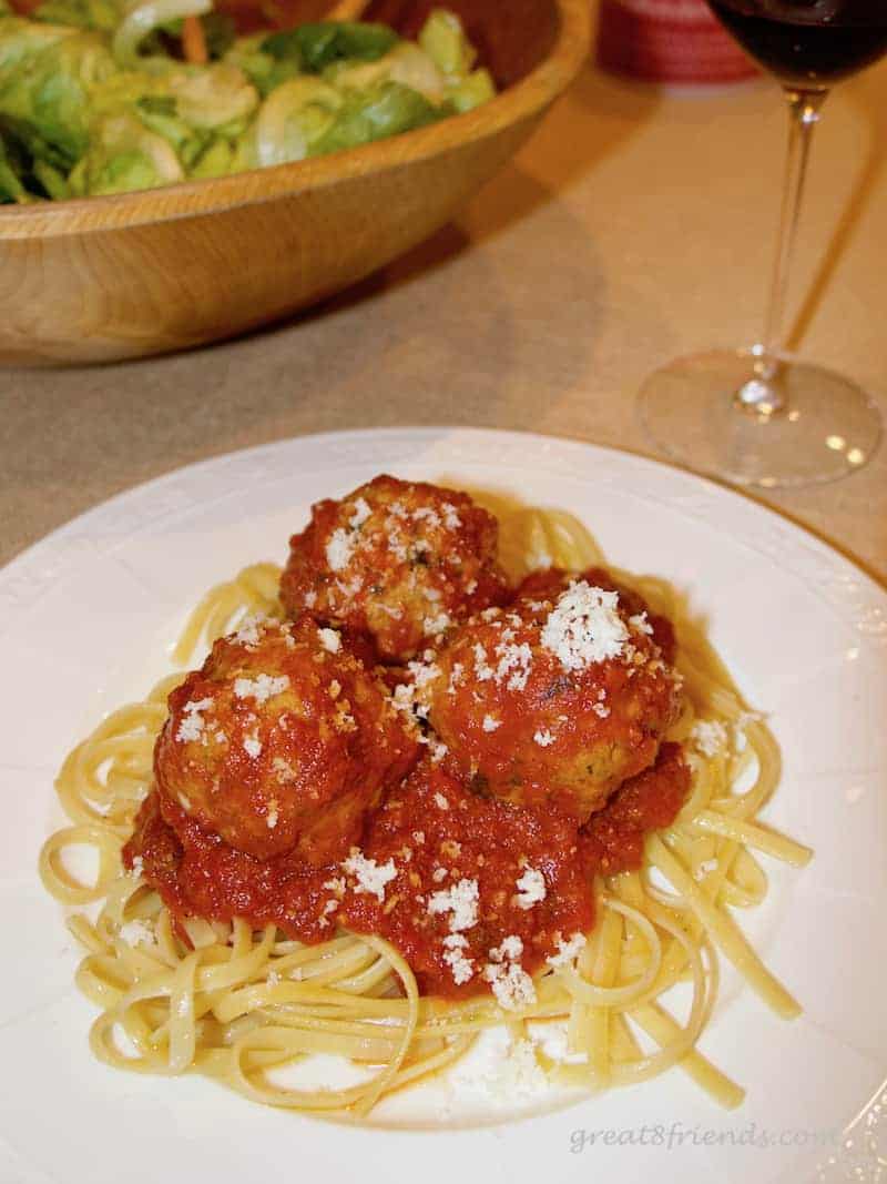 White plate of spaghetti and threee meatballs sprinkled with parmesan cheese.