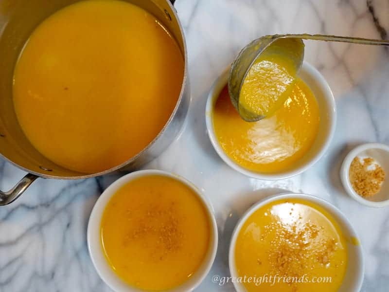 Butternut squash soup in a pot with four other small bowls filled with the light orange soup.