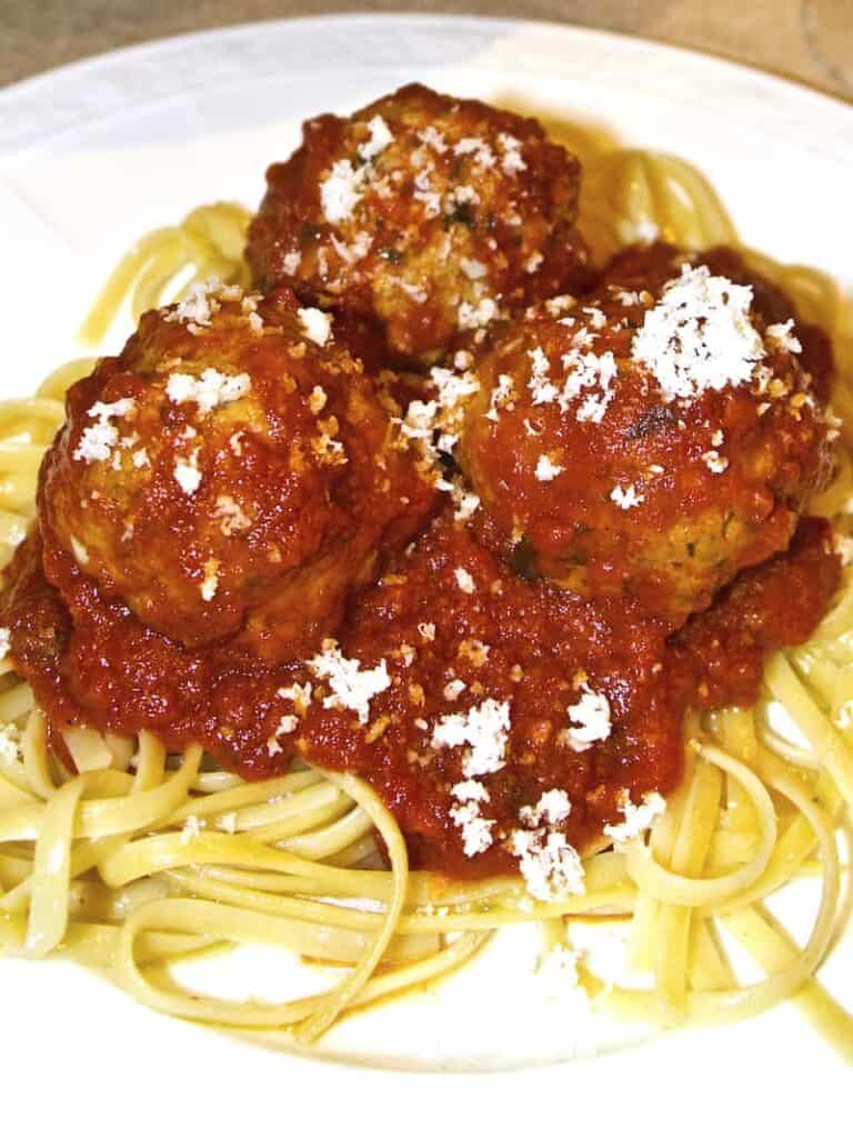 A plate of spaghetti with 3 meatballs and sauce.
