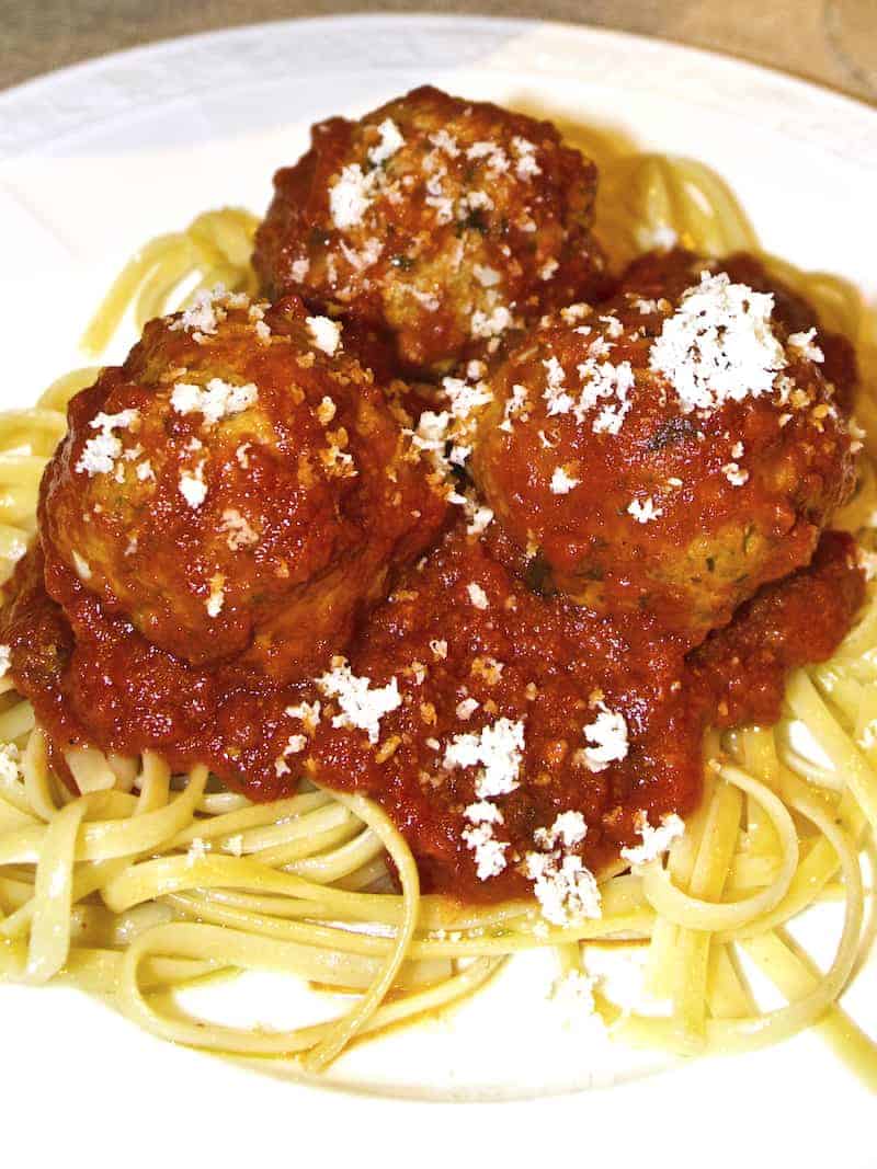 A plate of spaghetti with 3 meatballs and sauce.