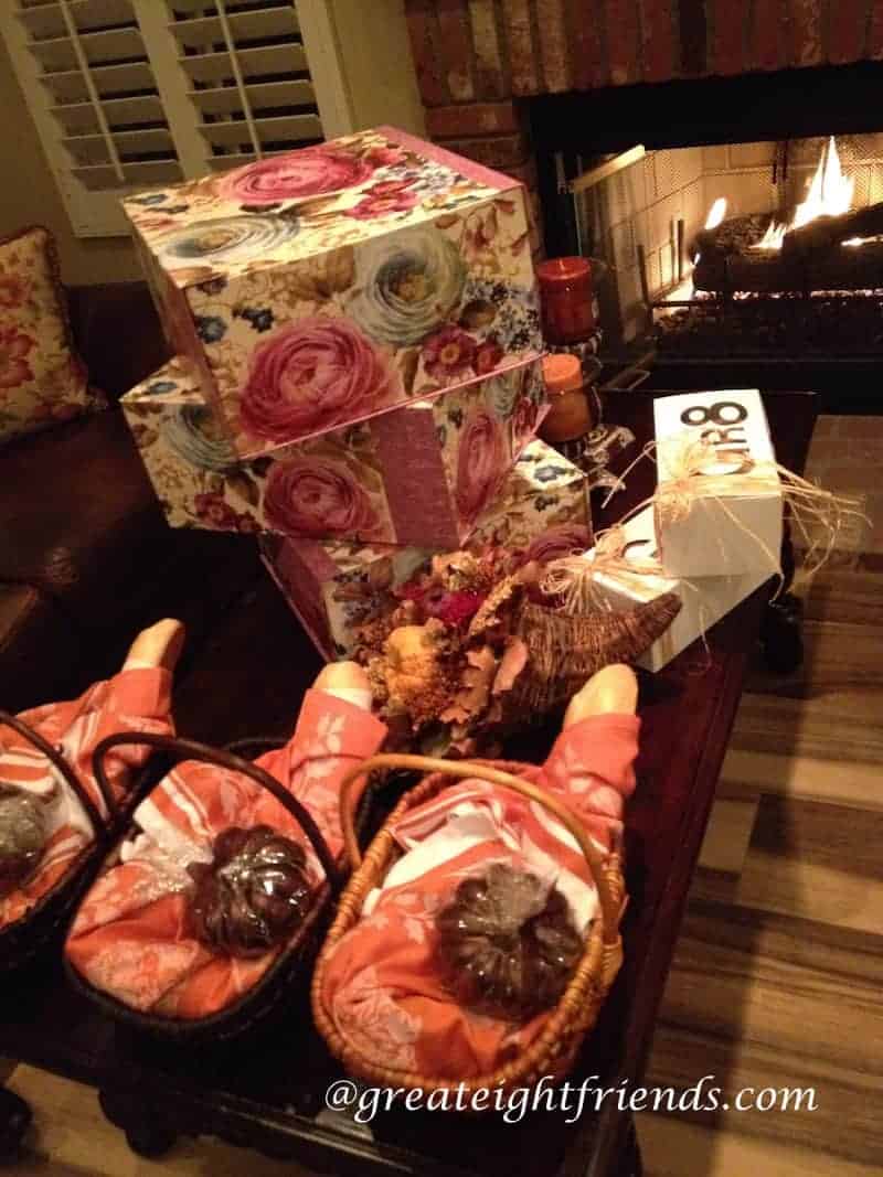 Many wrapped gifts on a table in front of a roaring fire in the fireplace.