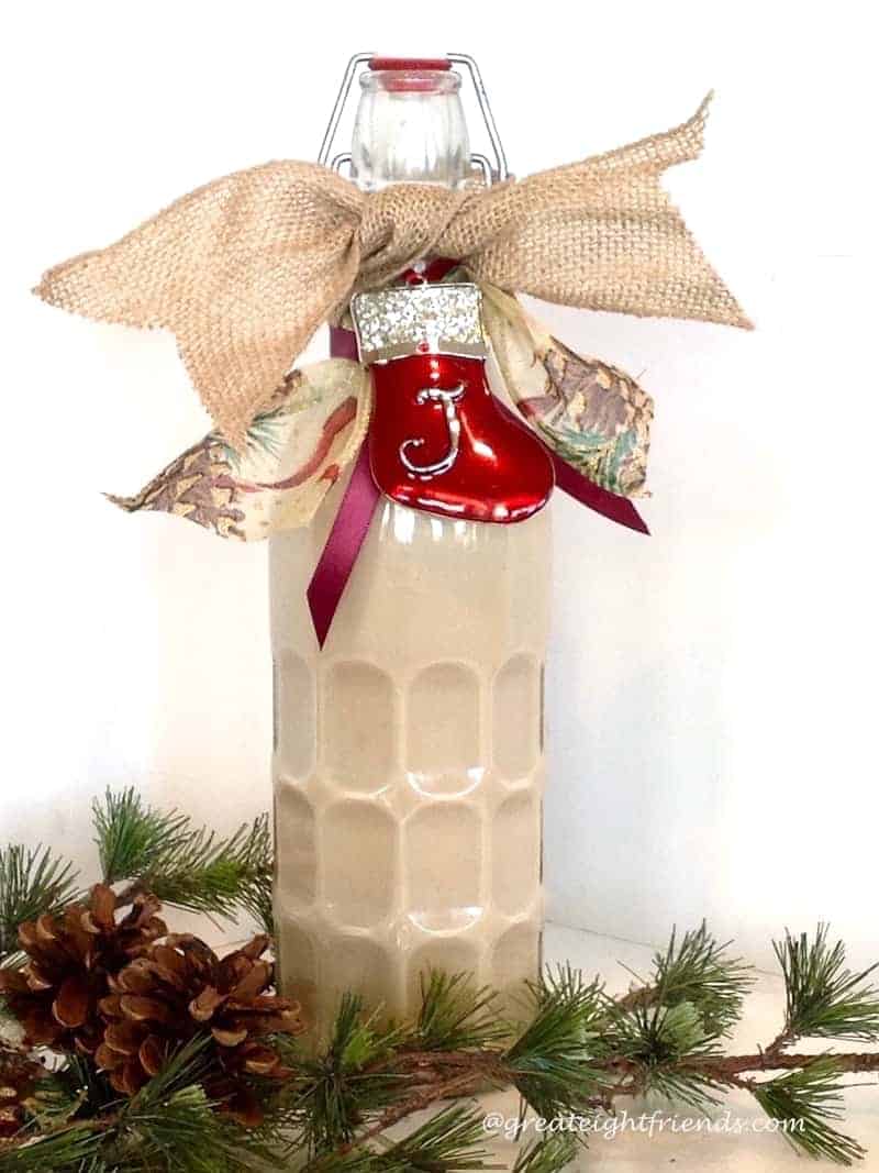 Homemade Irish Cream in a bottle decorated for Christmas with a ribbon and enamel ornament.