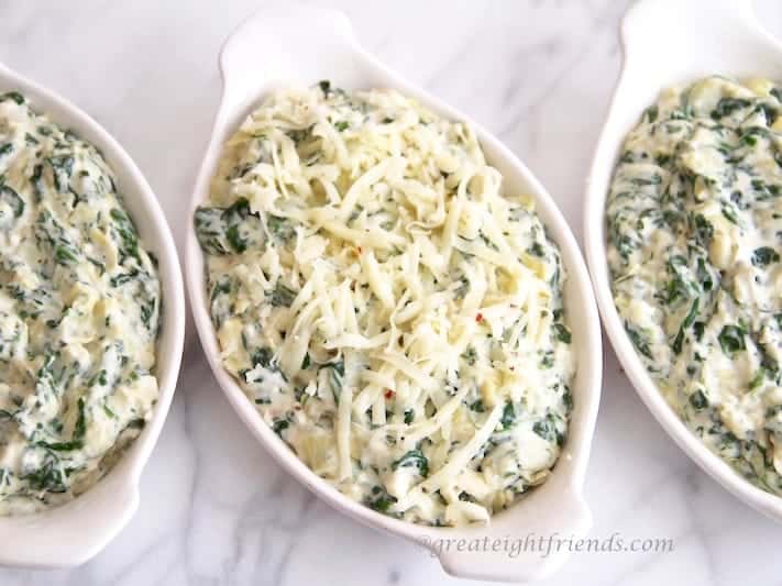 Spinach, artichoke and cheese dip served in three white ceramic dishes.