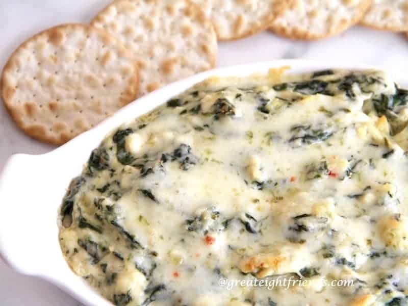 Spinach Artichoke Dip served in an oval white ceramic dish with crackers on the side