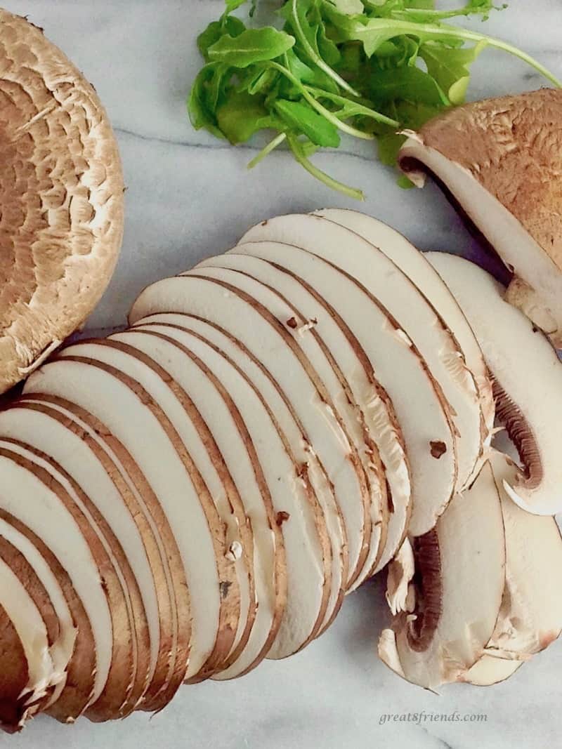 Sliced portobello mushrooms with a small amount of arugula on the cutting block.