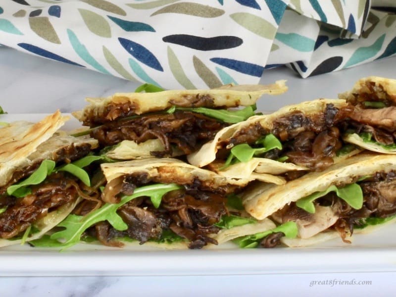 Portobello Mushroom Quesadillas with carmelized onions cut in half and stacked on a white serving platter.