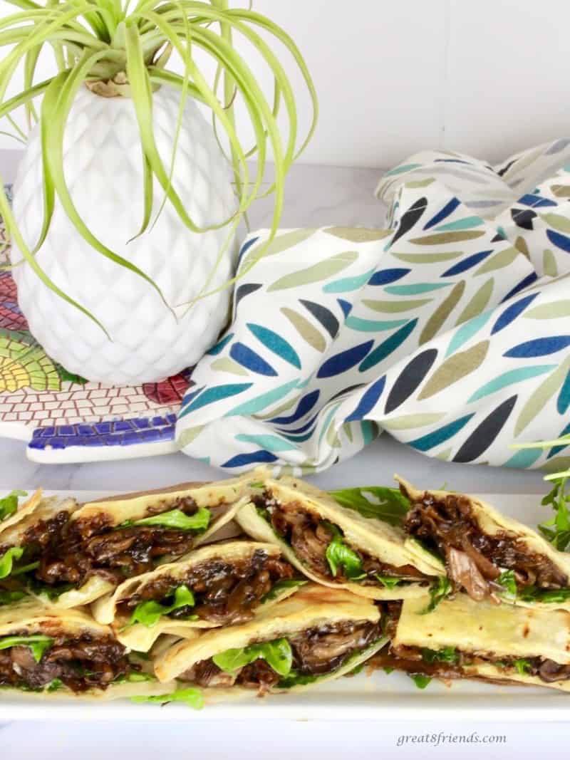 Quesadillas cut and stacked on a serving platter with a plant and colorful napkin in the background.