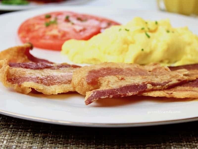 Slices of bacon, scrambled eggs and a slice of tomato on a plate.