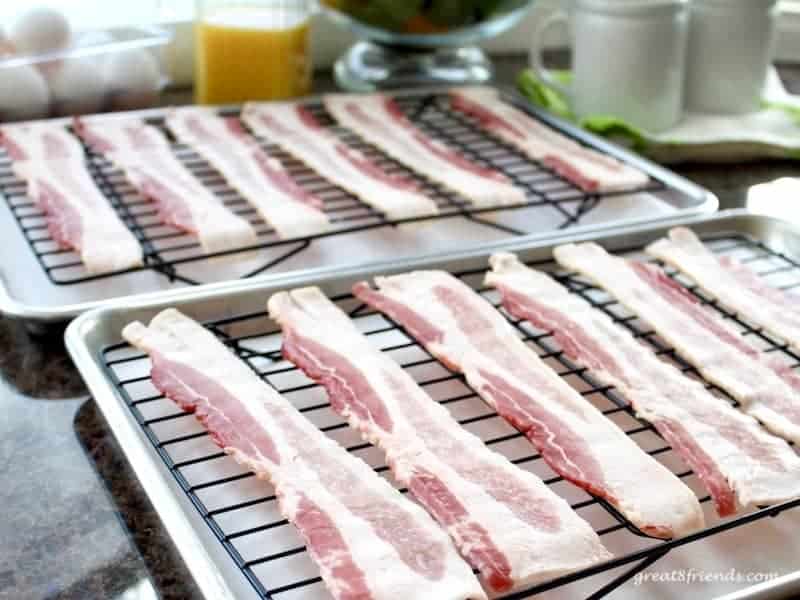 Uncooked bacon slices on two baking sheets.