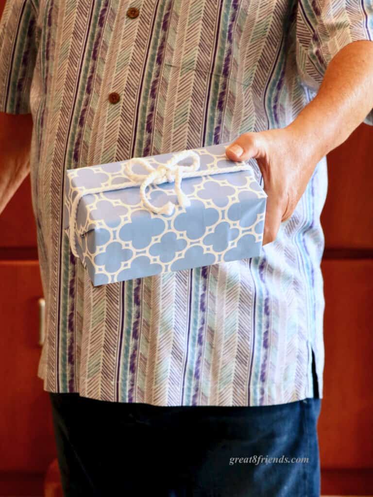 A man's hand holding a gift wrapped in blue and white paper with a white rope bow.